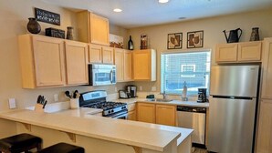 A kitchen with wooden cabinets, a stainless steel refrigerator, a stove, and a large island with bar stools.