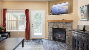 A living room with a stone fireplace, a television mounted above it, and a large window with curtains.