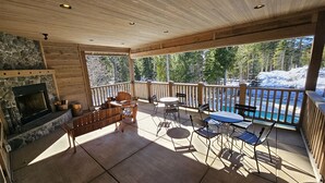 Une terrasse couverte avec une cheminée en pierre, des meubles en bois et une vue sur un paysage enneigé.