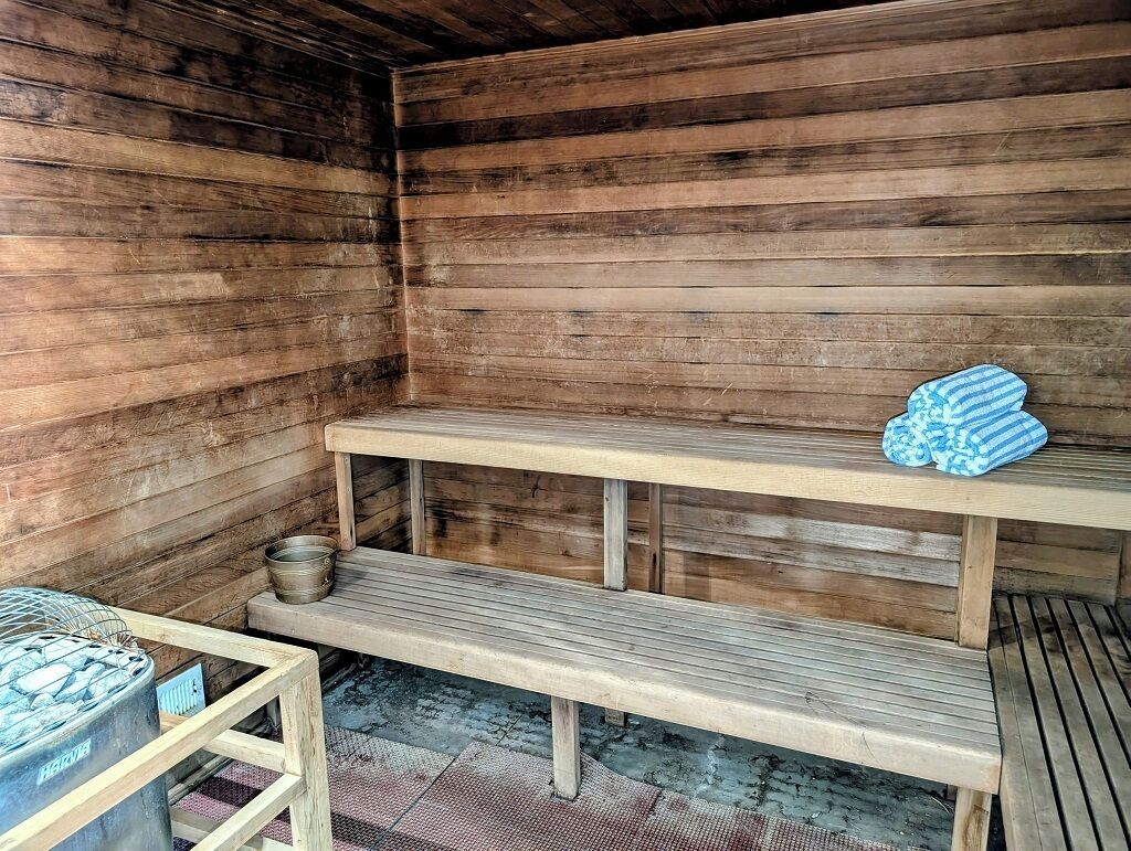 A sauna room with wooden benches and a metal container.