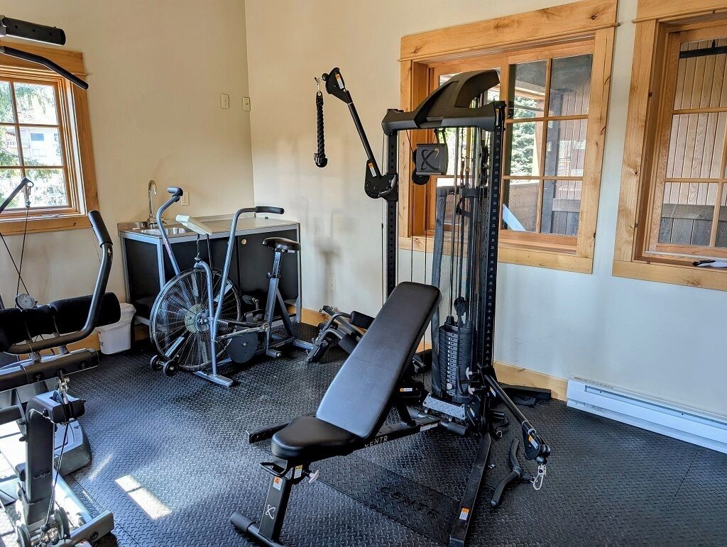 Ein Fitnessraum mit Trainingsgeräten, einer Bank und einem Fenster mit Holzrahmen.