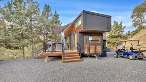 A modern cabin with a wooden deck, a covered outdoor area, and a golf cart.