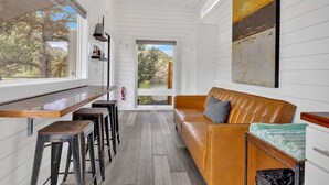 A modern interior with a wooden bar, leather sofa, and a large window offering a view of trees.
