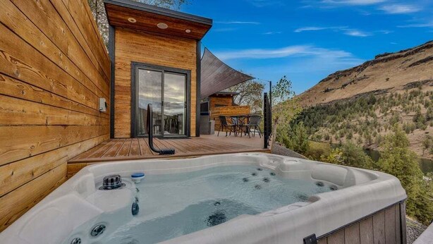 A wooden cabin with a hot tub and a deck overlooking a valley.