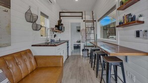 A compact kitchen with a wooden countertop, a brown leather sofa, and a bar area with stools.