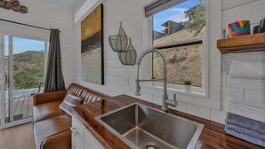 A modern kitchen with a wooden countertop, stainless steel sink, and a view of the desert landscape through large windows.
