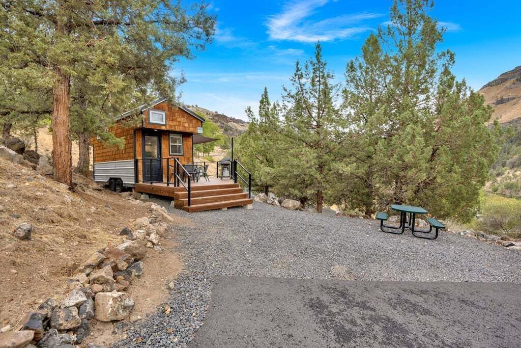 A cabin with a wooden exterior, a porch, and a picnic table in a forested area.