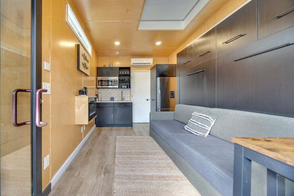 Una cocina compacta con electrodomésticos modernos, un sofá gris y una mesa de madera.