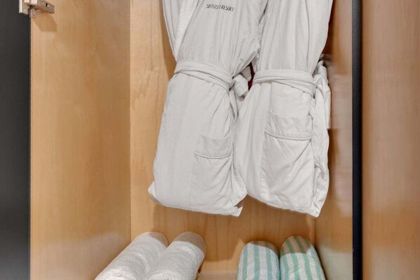 A wooden door with two white robes hanging on hooks and a pair of striped slippers on the floor.
