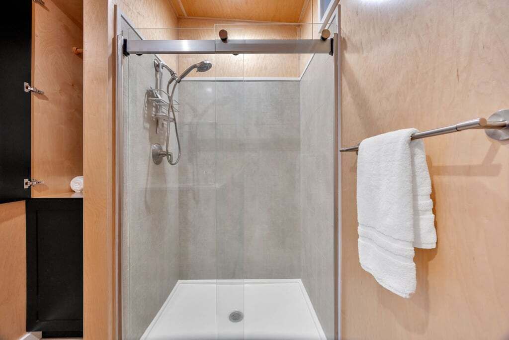 A shower with a glass door, a towel rack, and a wooden panel wall.