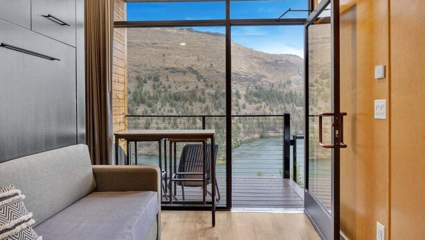 Una camera moderna con un divano, un tavolino e una sedia. Dispone di un'ampia porta vetrata che dà su un balcone con vista su un fiume e montagne.