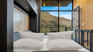 Camera con un'ampia finestra vista sulle montagne, un letto con lenzuola bianche e soffitto in legno.
