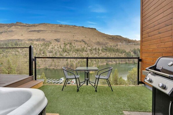 Un patio con jacuzzi, parrilla y mesa con sillas con vista a un lago y colinas.