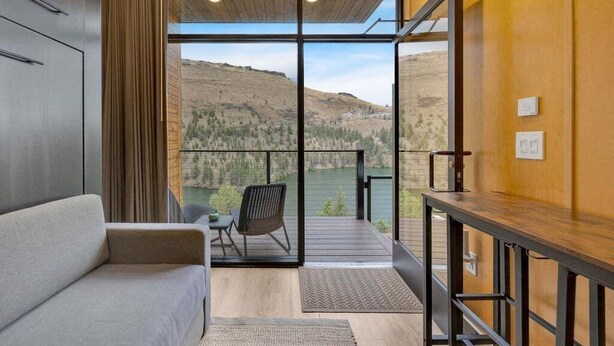 Una habitación moderna con sofá, mesa de comedor y vistas a un lago y montañas a través de amplios ventanales.