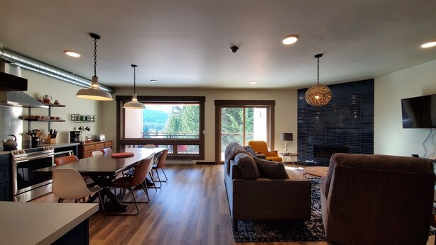 Una cocina moderna con comedor, una sala de estar con sofá y televisor, y ventanas amplias que ofrecen vistas al exterior.