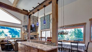 Una cocina amplia con una isla grande, vigas de madera, detalles de piedra y lámparas colgantes.