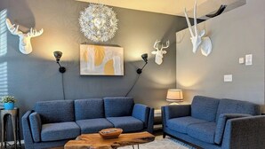 Een moderne woonkamer met twee blauwe banken, een houten salontafel en decoratieve wanddecoratie van gewei.