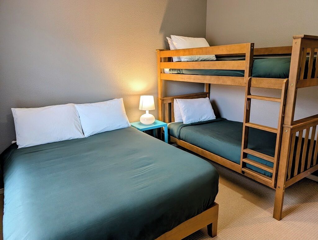 A room with two bunk beds, a bedside table with a lamp, and a bed with pillows.
