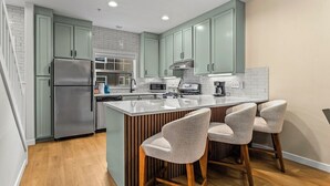 Una cocina moderna con armarios verde claro, un refrigerador de acero inoxidable, un microondas y una isla grande con taburetes de bar.