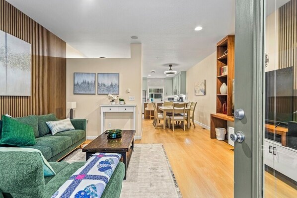 A modern living room with a green sofa, a wooden coffee table, and a dining area with a table and chairs. - Chalet 100 at the Official Collins Lake Resort (Government Camp)