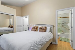 A bedroom with a large bed, a mirror, a door leading to a bathroom, and a small table with a lamp. - Chalet 100 at the Official Collins Lake Resort (Government Camp)