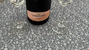 Eine Flasche Lindauer Brut Champagner mit zwei leeren Gläsern auf einer gemusterten Tischdecke.
