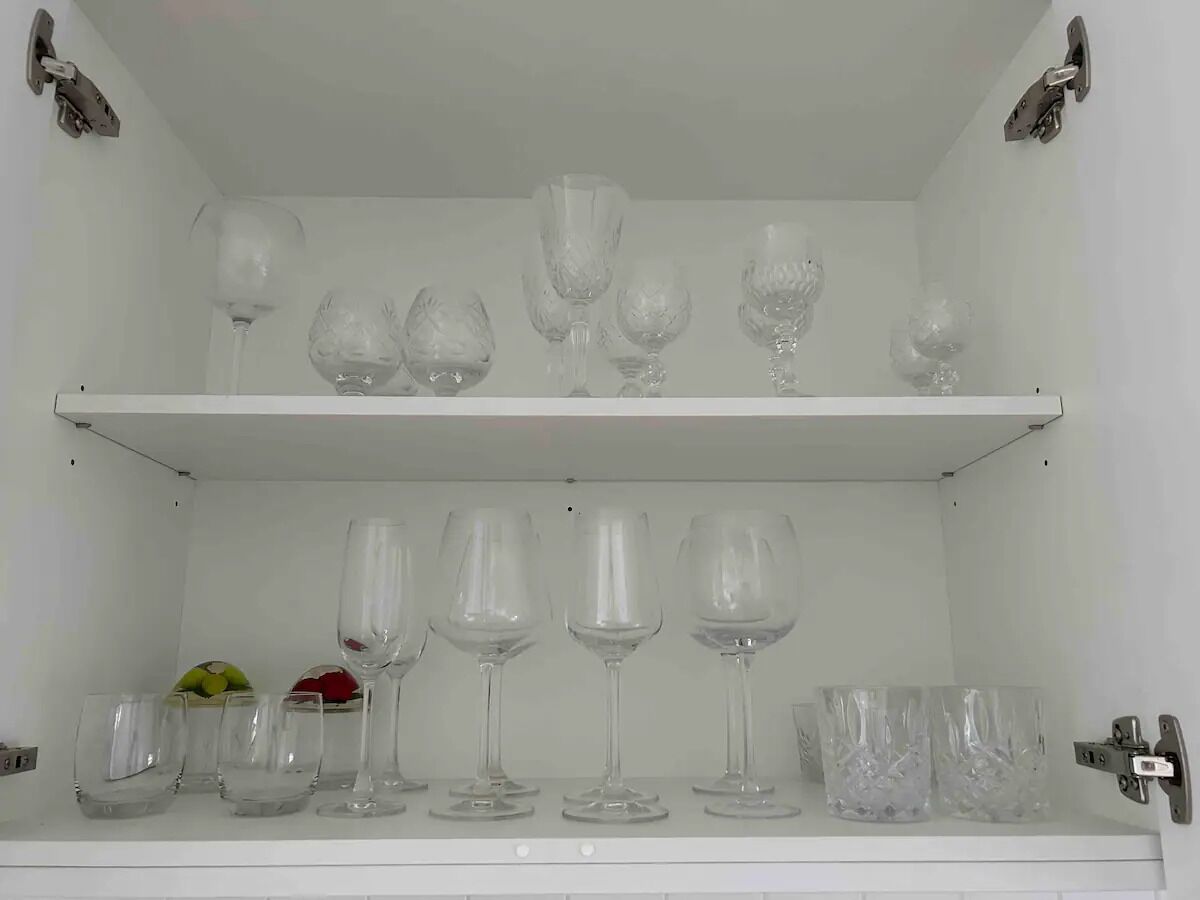 Un estante blanco con diferentes tipos de cristalería, incluyendo copas de vino y vasos, organizados cuidadosamente.