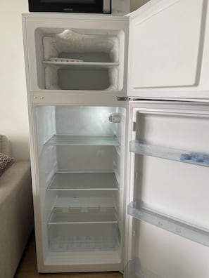 An open refrigerator with multiple shelves and a microwave above it.