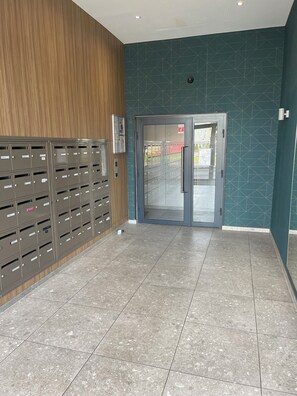 Una hall con una fila di cassette postali, un pannello di legno e una parete color acquamarina con motivi geometrici.
