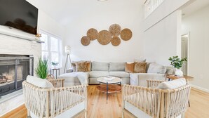 Ein modernes Wohnzimmer mit Kamin, einer großen Couch, zwei Sesseln, einem Couchtisch und einem Wandbild.