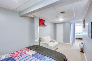 Ein Schlafzimmer mit einem Bett, einem weißen Sessel, einem roten Vorhang und Blick auf einen Strand durch eine geöffnete Tür.