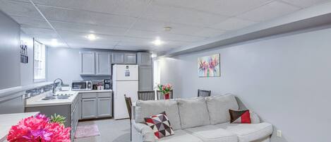 A compact living space with a kitchenette, a sofa, a small table, and a vase of flowers.