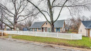 Une rue résidentielle bordée de maisons, avec une clôture blanche en bois et des arbres sans feuilles.