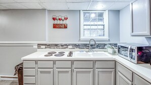 Une cuisine avec un plan de travail blanc, un évier, un four à micro-ondes et une fenêtre équipée de stores.
