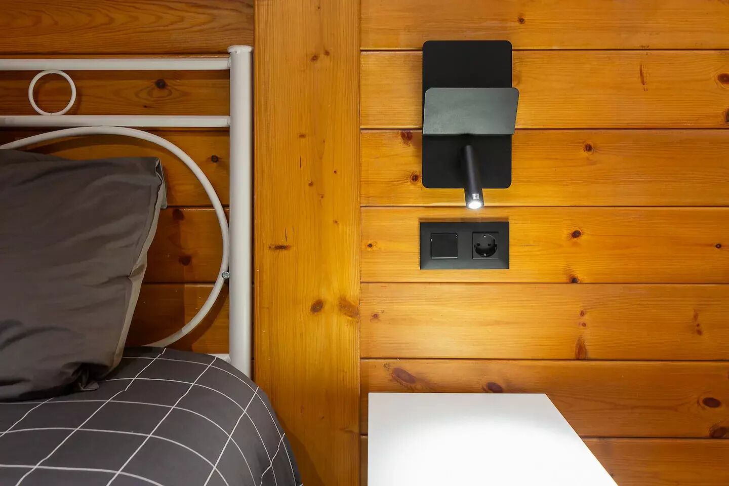 Una camera arredata in stile baita, con un letto, un lampadario bianco fissato al muro e una presa di corrente.