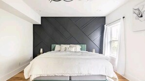 A modern bedroom with a large bed, a geometric wall design, and a window with curtains. - Stunning Home Getaway
Modern house with a rooftop / 6 minute from Broadway (Nashville)