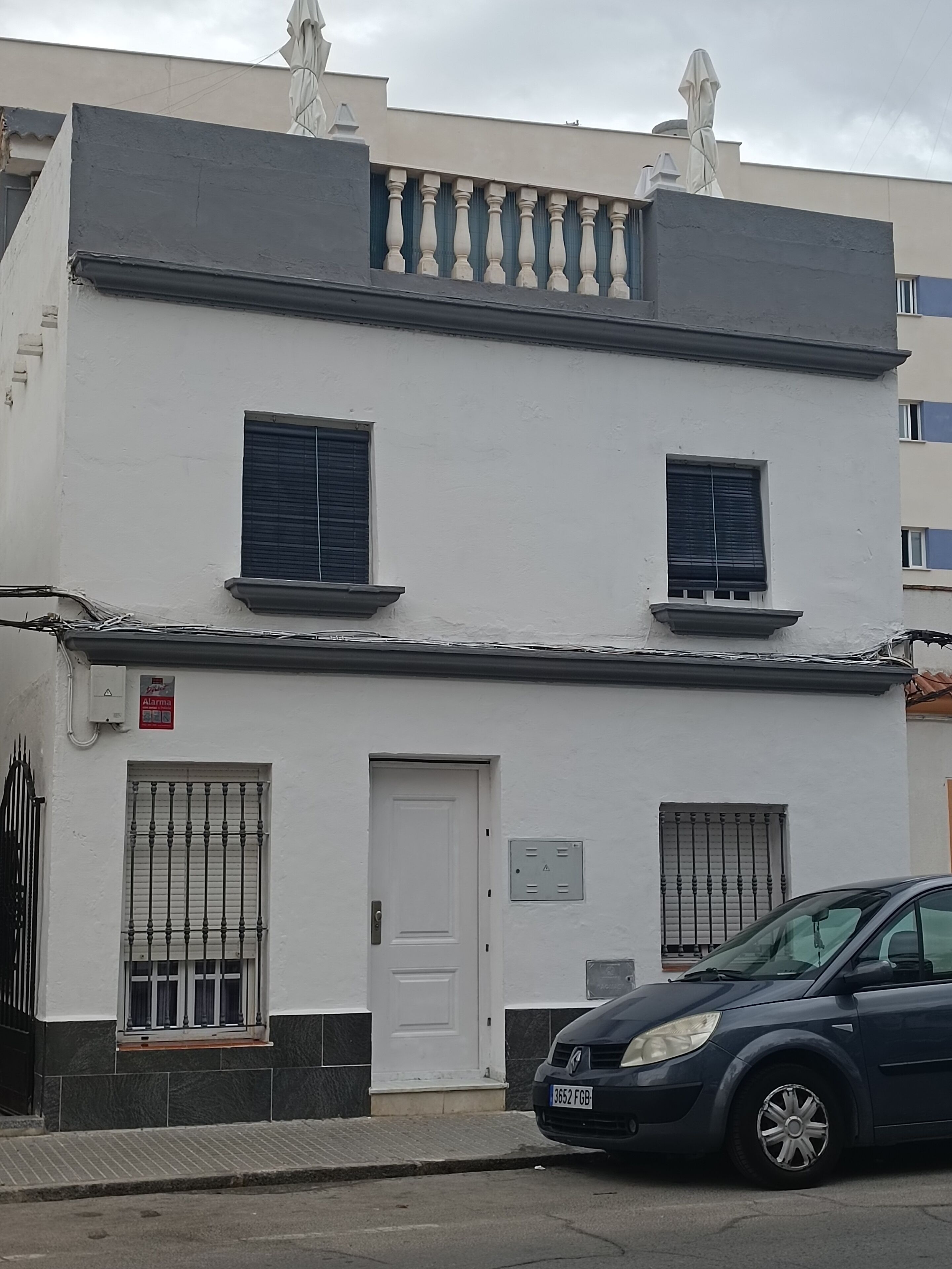 Un edificio de dos pisos con fachada blanca, una puerta negra y ventanas con barrotes.