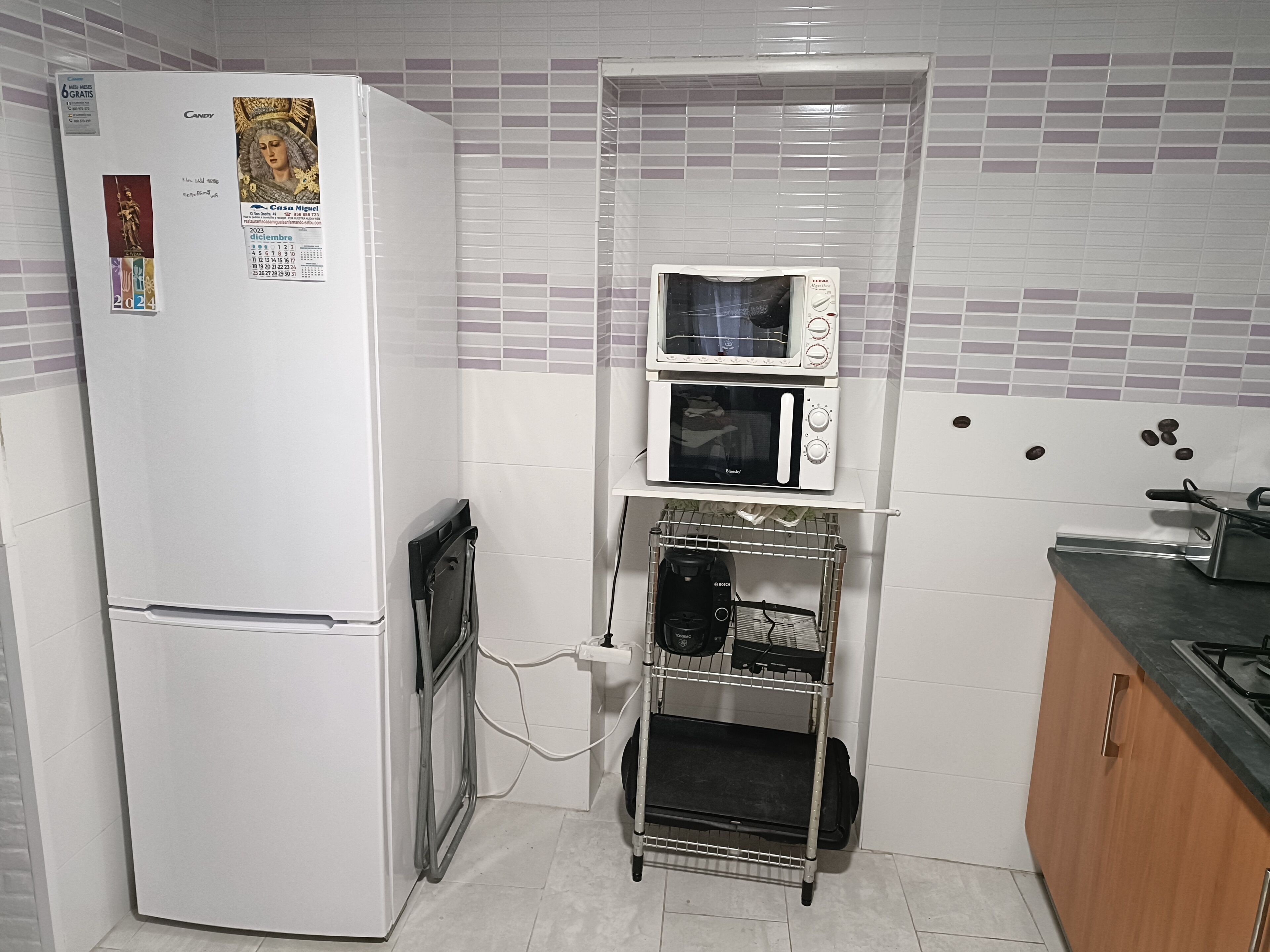 Een compact keukenmeubilair met een koelkast, een magnetron en een koffiezetapparaat op een plank.