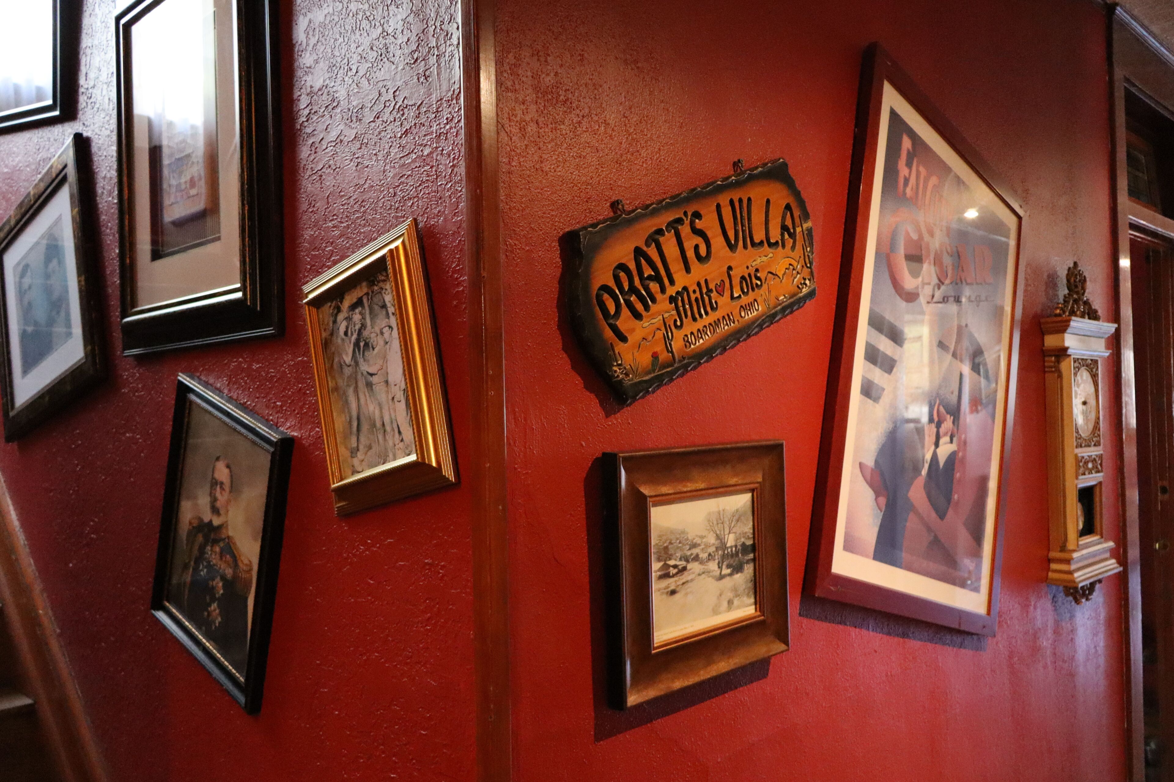 A wall with multiple framed photographs and a sign that reads 'Pratts Villa Boardman, Ohio.'