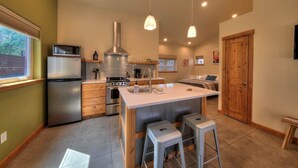 A modern kitchen with a central island, stainless steel appliances, pendant lighting, and a wooden door. - Casa Moab Hideaway | Downtown | Sauna and Fire Pit (Moab)