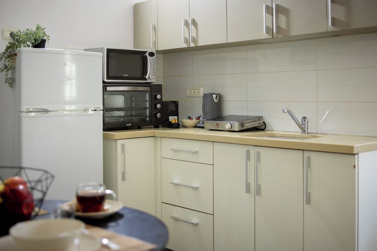 A kitchen with a refrigerator, microwave, oven, coffee maker, and a sink.