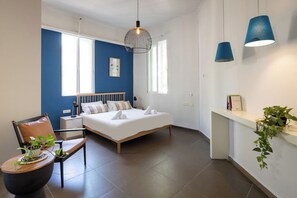 A modern bedroom with a bed, bedside tables, a chair, a hanging light fixture, and a window. - The Printhouse Boutique Studio 2 by SeaNRent (Haifa)