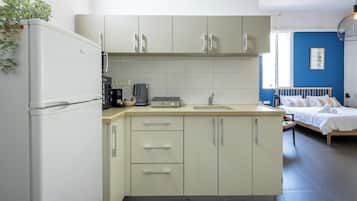 A compact kitchen with a refrigerator, microwave, and coffee maker. A bed with a wooden headboard is visible in the adjacent room.
