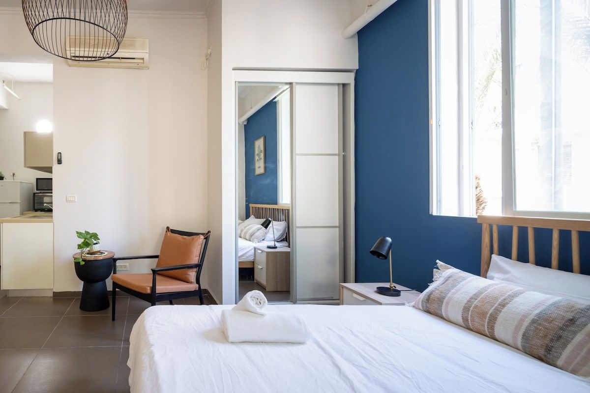 A hotel room with a bed, a chair, a desk, a lamp, and a view of the outside.