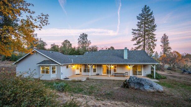 A single-story house with a covered porch, a front yard with a large rock, and a clear sky. - Lupine Landing (Mariposa County)