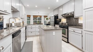 A modern kitchen with white cabinetry, granite countertops, stainless steel appliances, and a large island. - Lupine Landing (Mariposa County)