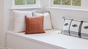 A room with a built-in bench along a large window, two hanging macramé planters, and a view of a natural landscape. - Lupine Landing (Mariposa County)