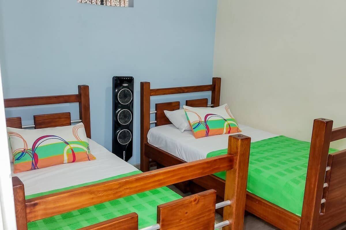 A room with two wooden beds, each with a green mattress and colorful pillows.