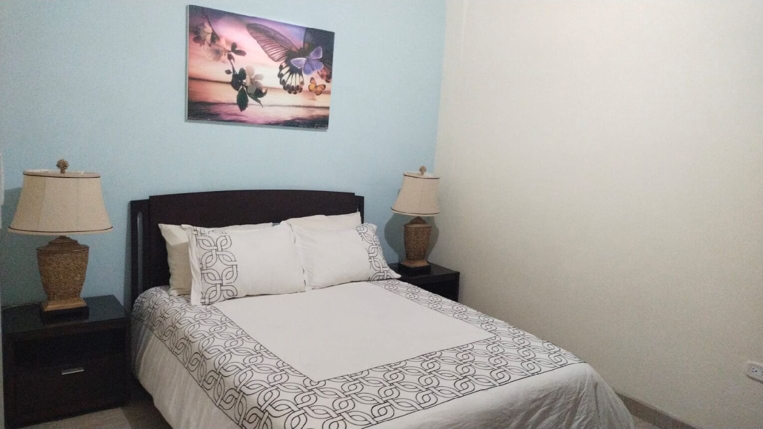 A neatly made bed with a patterned bedspread, two bedside lamps, and a wall-mounted picture.