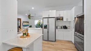 Une cuisine moderne avec des meubles blancs, un réfrigérateur en acier inoxydable, une cuisinière et un plancher en bois.